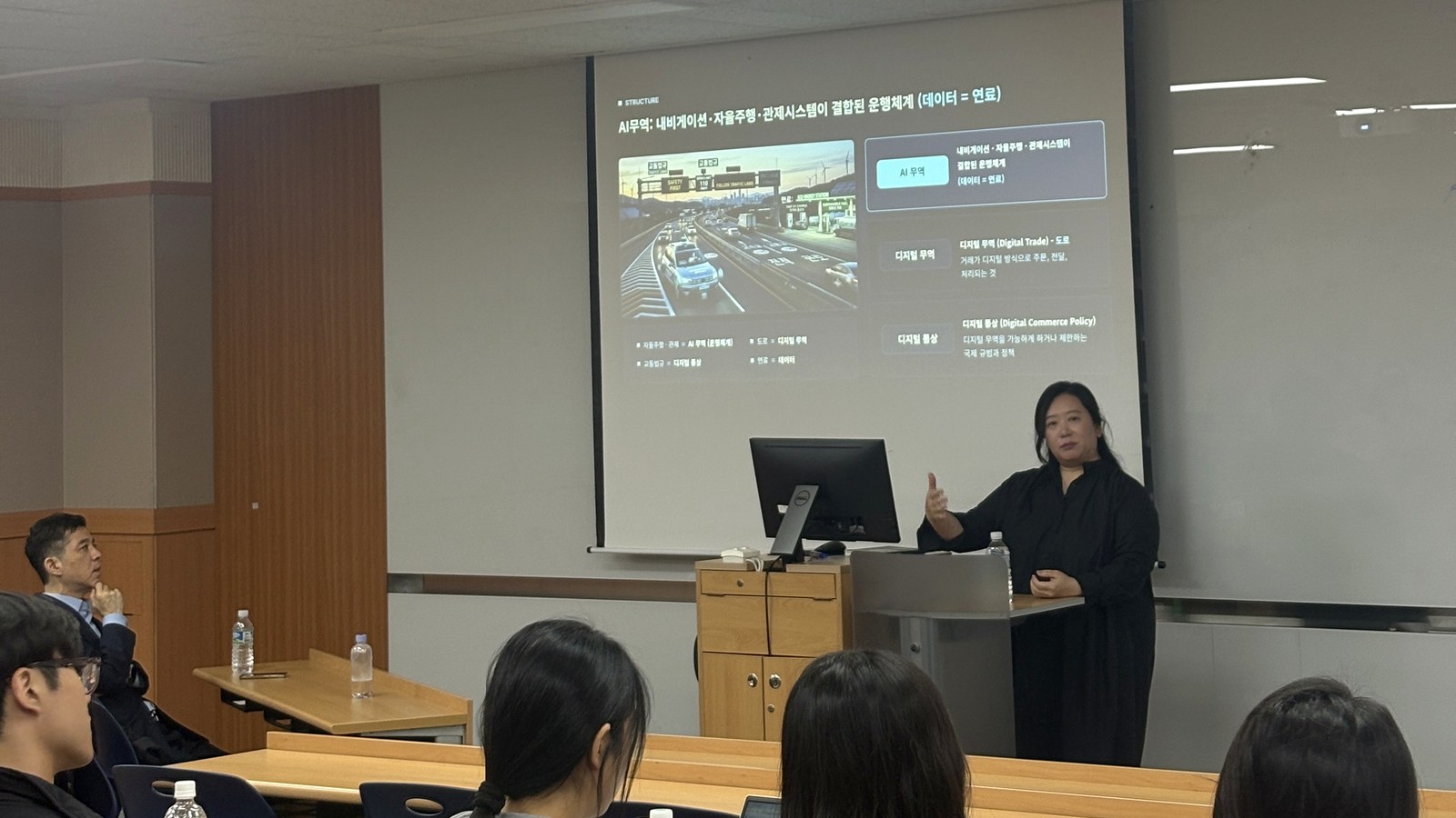 Songyi Yang beside an AI trade presentation screen with Kyung Hee GTEP students listening in the front row