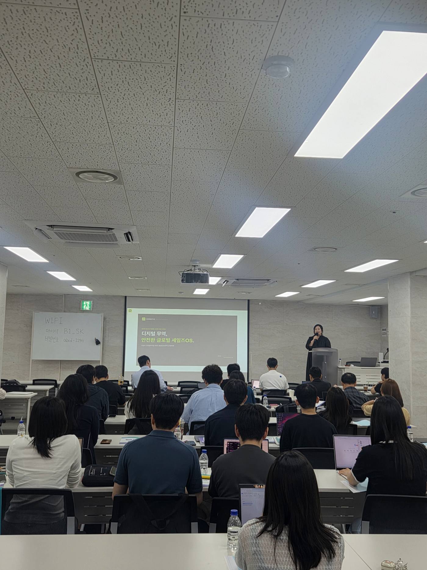 A digital trade lecture slide on the screen at the front of the room while participants follow along on their laptops